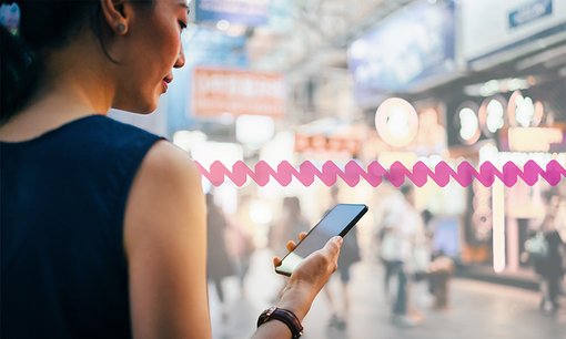 Woman using smartphone in busy city street, against colorful neon commercial sign and city buildings